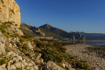 Naklejka premium A beautiful sunset over the warm sea to which rocky mountain peaks and walls descend.