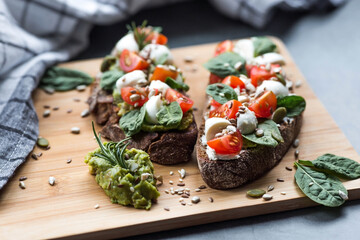 Bruschetta (sandwiches) with cherry tomatoes, mozzarella cheese and herbs on a cutting board on a dark background. Traditional Italian snack.