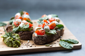 Bruschetta (sandwiches) with cherry tomatoes, mozzarella cheese and herbs on a cutting board on a dark background. Traditional Italian snack.