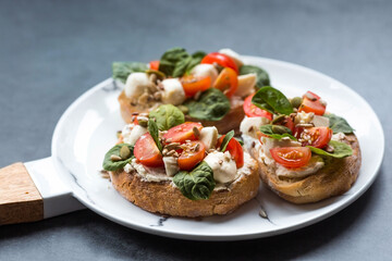 Bruschetta (sandwiches) with cherry tomatoes, mozzarella cheese and herbs on a stylish plate on a dark background. A traditional Italian snack.