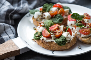 Bruschetta (sandwiches) with cherry tomatoes, mozzarella cheese and herbs on a stylish plate on a dark background. A traditional Italian snack.