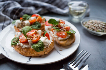Bruschetta (sandwiches) with cherry tomatoes, mozzarella cheese and herbs on a stylish plate on a dark background. A traditional Italian snack.