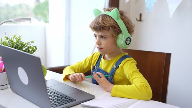 Cute smart caucasian primary School Child with headphones educate online laptop. Tutor teaching digital class, web lesson on computer at home. Virtual education. Schoolboy girl studying doing homework
