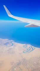 View from the window of plane on blue sky and earth with landscape of desert, sea and canals in Emirates