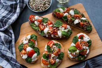 Bruschetta (sandwiches) with cherry tomatoes, mozzarella cheese and herbs on a cutting board on a dark background. Traditional Italian snack.