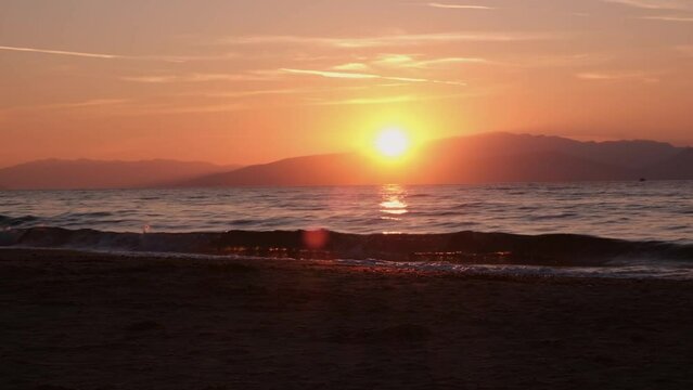 Stunning stock video footage of the sun setting behind the mountains, with glistening waves of the sea in the foreground