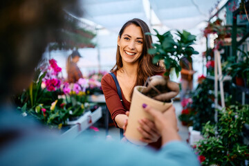 Young happy woman buys potted plant in garden center.