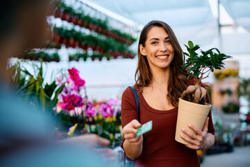 Happy woman pays with credit card at garden center.