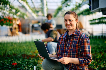 Happy plant nursery worker using laptop and looking at camera.