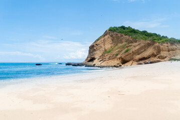 clam and flat beach of hard packed soft white powdery sand with an exposed rocky cliff that has been weathered and eroded in the distance forming a sheltered bay