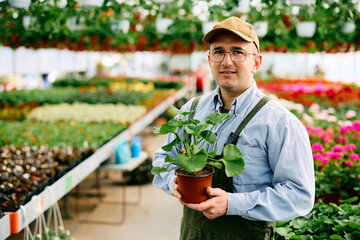 Small business owner with flower pot in plant nursery looking at camera.