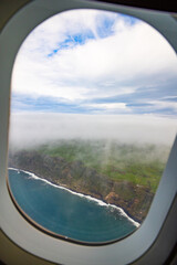 Photo taken out the window of plane, view over island with ocean and clouds.