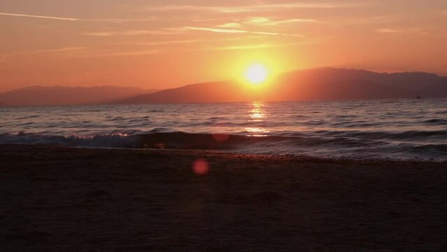 Stunning stock video footage of the sun setting behind the mountains, with glistening waves of the sea in the foreground