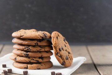 chocolate chip cookies on wooden table, stack of chocolate chip cookies on a wooden table, chocolate chip cookies on top of white dish towel on a white wooden table