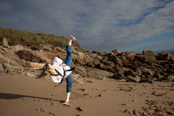 woman doing taekwondo on the beach giving a kick to the air
