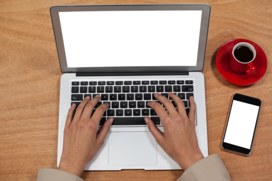 Businesswoman using laptop with coffee and mobile phone on desk