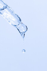 Cosmetic pipette with dripping liquid and drops on a blue background, serum, serum, gel, vitamin, water, oil. Clean, fresh, moisturizing