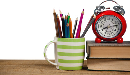 Books with alarm clock by colored pencils in mug on table
