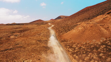 Car driving on empty dirt road in desert volcanic landscape at summer sunny day. Fuerteventura Canary Island Spain.