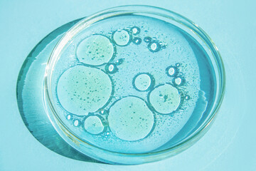 Petri dish. Petri's cup with liquid. Chemical elements, oil, cosmetics. Gel, water, molecules, viruses. Close-up. On a blue background.