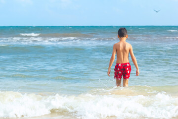 A boy is walking in the water at the ocean beach on vacations.