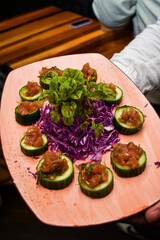 a platter of cucumbers with cevice on top being passed around at a party as an appetizer
