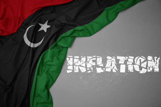 waving colorful national flag of libya on a gray background with broken text inflation. 3d illustration