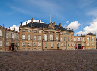 Fototapeta na wymiar Copenhagen, Denmark - September 13, 2010: King Christian 8 brown stone palace with black roof at Amalienborg square under blue sky. Statues, pillars and windows. Red guard stations add color