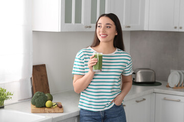 Beautiful young woman holding glass with tasty smoothie in kitchen