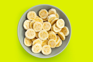 Banana slices in bowl on green background.