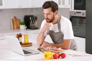 Fototapeta na wymiar Man making dinner while watching online cooking course via laptop in kitchen