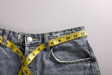 Jeans with measuring tape on light grey background, top view and space for text. Weight loss concept