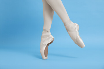 Young ballerina in pointe shoes practicing dance moves on light blue background, closeup