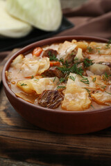 Tasty cabbage soup with meat, carrot and dill on wooden table, closeup