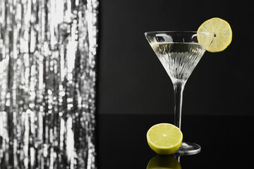 Martini cocktail with lemon slice on black and silver background, space for text