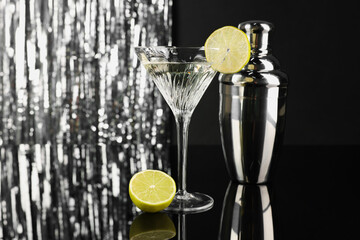 Martini cocktail with lemon slice and shaker on black and silver background