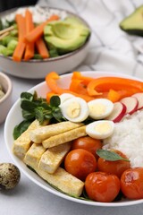 Delicious poke bowl with basil, vegetables, eggs and tofu on light grey table