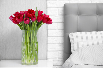 Bouquet of beautiful tulips in glass vase on white nightstand near bed