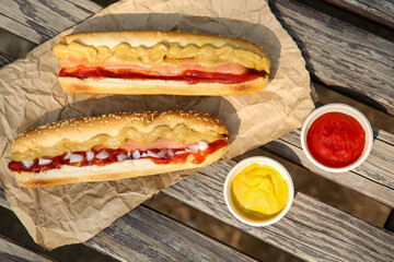 Fresh delicious hot dogs and sauces on wooden surface outdoors, flat lay