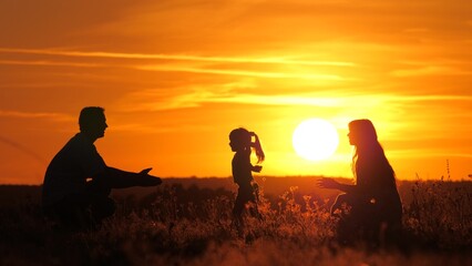 Fototapeta na wymiar Child plays with parents. Kid runs from mom to dad, hugs and kisses his parents at sunset. Happy family walks in park with their daughter in sun. Father, mother, child, healthy family playing in field
