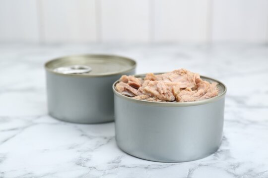 Tin cans with canned tuna on white marble table, closeup