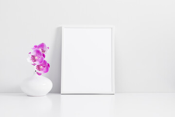 Empty pink photo frame mockup, pink orchid flowers in vase on white table background. Front view