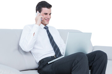 Businessman using mobile phone and laptop while sitting on sofa