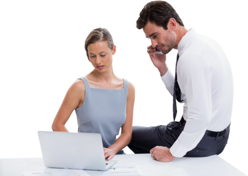 Businessman talking on phone while discussing with colleague over laptop against white background