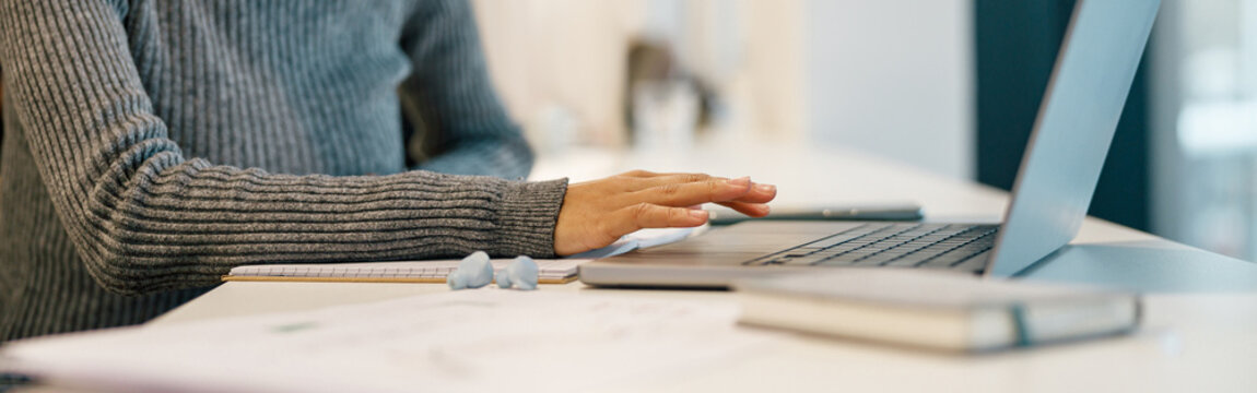 Smiling woman freelancer working laptop and making notes while sitting near windows in cozy cafe