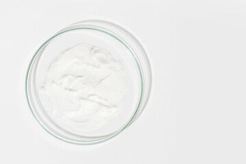 Petri dish on a light background. With a smear of white cream. Cosmetic cream, face mask, cream texture. View from above