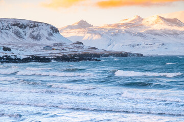 Snowy Mountains at Winter, Sunrise with Fluffy Clouds and Stormy Sea in Iceland. Landscape in North Europe Country. Atlantic Ocean Coast and Icelandic Fjords.