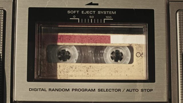 The cassette is played in the tape recorder. Close-up. Yellow audio cassette in deck playing and rotates. Vintage sound recording in old retro recorder. Call recording. Audiocassette playback. Macro
