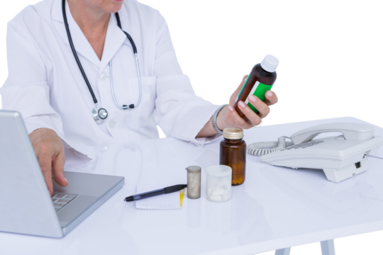 Female doctor holding pill bottle while using laptop