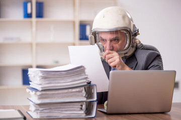 Old male employee wearing spacesuit in the office